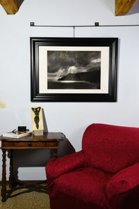 Framed Spotlight charcoal drawing of dramatic skies with sun rays dropping down on cliffs and coastline of Italy, shown here on wall in a small Tuscan living room