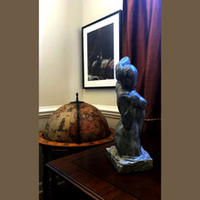 Laden Sie das Bild in den Galerie-Viewer, World Traveler Pinocchio Globe Map Old World Pastel Drawing shown here in a study with a globe bar and a stone carving Gemini also by artist Kelly Borsheim
