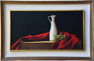 Green olives sit in a transparent bowl next to a tall thin white karaf containing olive oil.  A red cloth surrounds them as they sit on a warm wood box for used for wine transport.