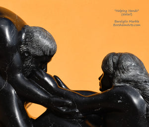 Detail of faces and the hands reaching for the man's face. Black marble figure sculpture detail of Helping Hands