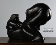 Cargar imagen en el visor de la galería, Her face and long hair Helping Hands by Kelly Borsheim Couple Art Carved from a black marble called Bardiglio from Italy, this sculpture depicts a man bending over forward to help a seated woman stand up.  Her hands reach up towards his bearded face, but it is the moment before she is close enough to reach him. 
